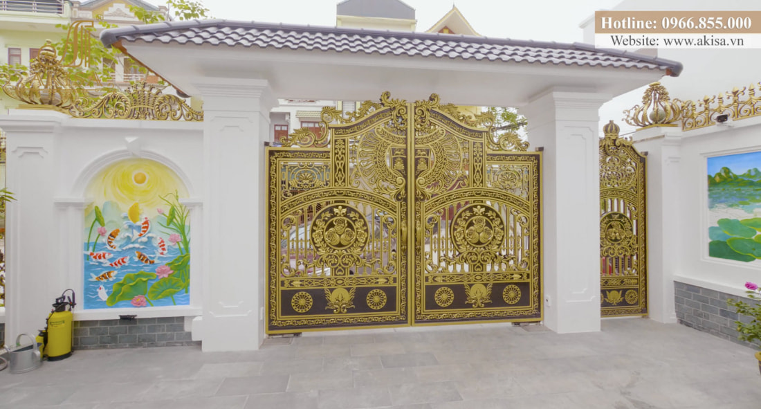 Cổng chính nổi bật với cột trụ bê tông khỏe khoắn, bề thế cùng cánh cửa bằng nhôm đúc nghệ thuật màu vàng đồng sang trọng, quý phái